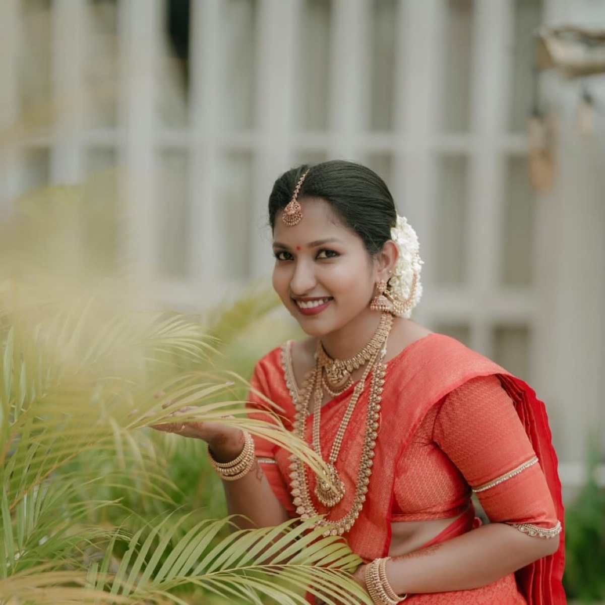 A bride in a coral silk saree with gold jewellery and jasmine