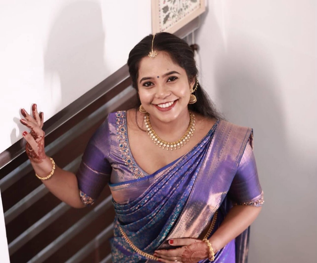 A smiling bride in a purple silk saree with gold jewellery