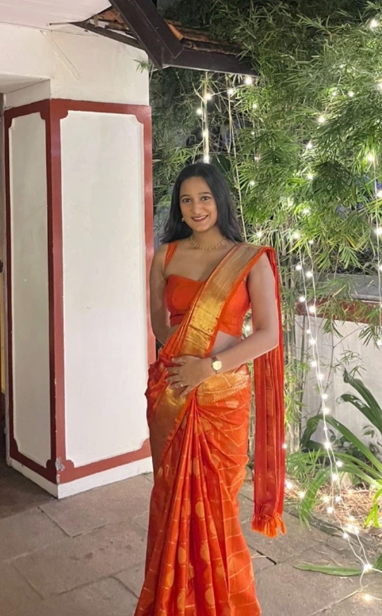 A client in an orange saree in front of a lit house at night