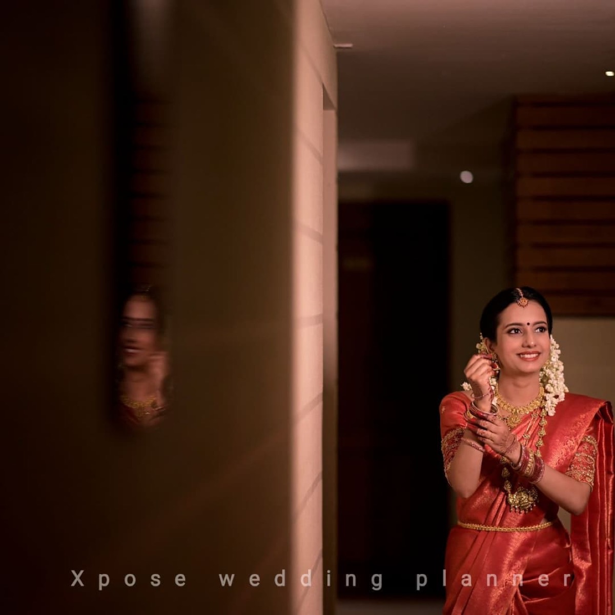 A bride in a red silk saree with jasmine and gold jewellery, fixing her earring