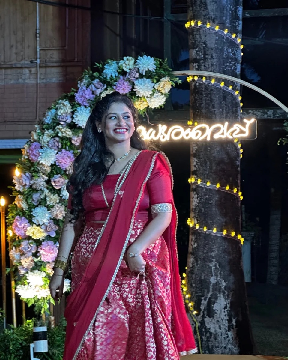 A bride-to-be in red at an evening madhuram vaipu, under a flower arch