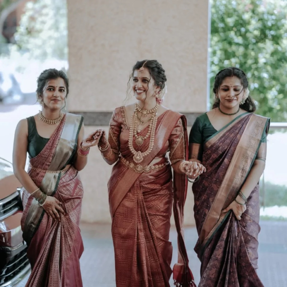 A bride walking in with two bridesmaids, all in maroon silk